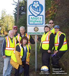 Proud Volunteers standing by a local Adopt a Highway sign