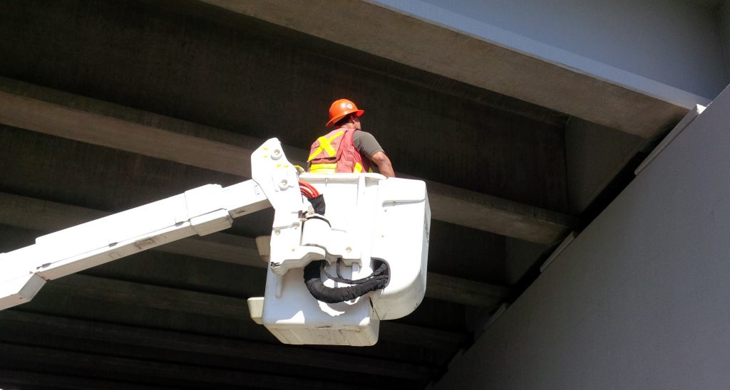 Bridge inspector inspecting a bridge, in a utility bucket truck