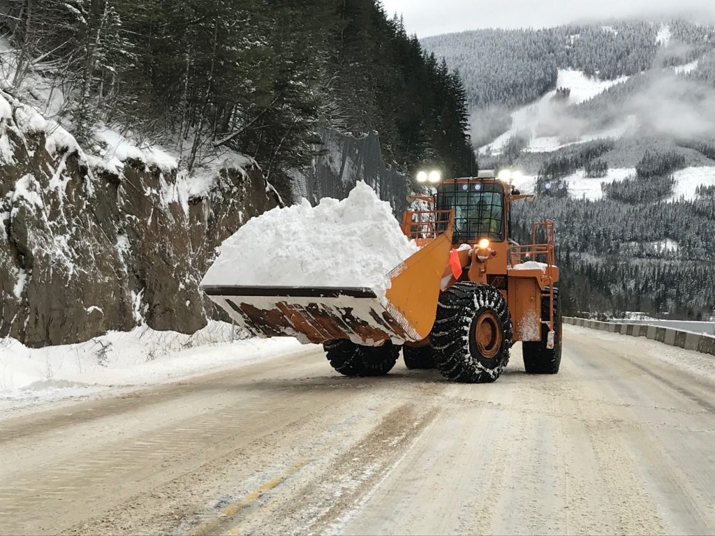 Front-end Loader with snow bucket clearing snow from a BC highway.