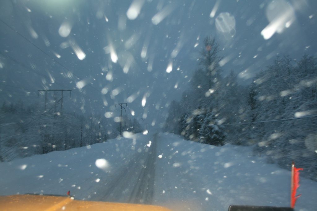 A snapshot taken from the front of a plow at work during a snowstorm on a BC highway.