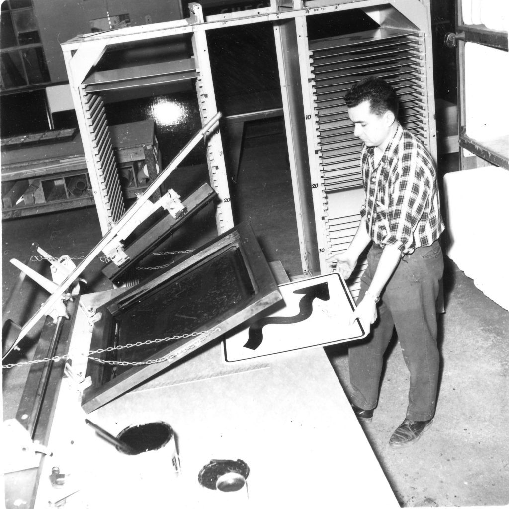 A ministry employee at the Provincial Sign Shop screen-printing a sign, using a manual production table.