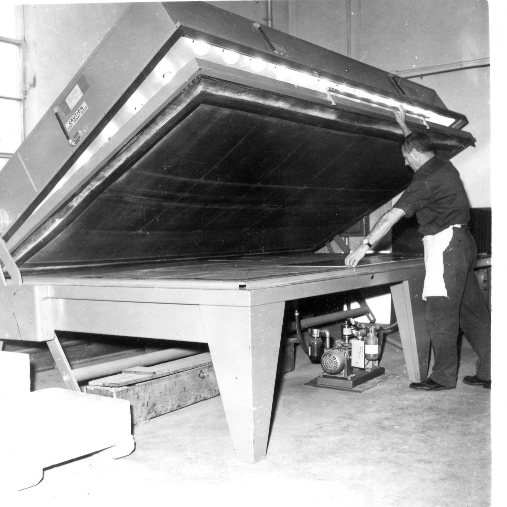 A ministry employee at the Provincial Sign Shop baking a heat activated reflective sign face onto a satin coat steel sign blank, using a heat vacuum applicator.