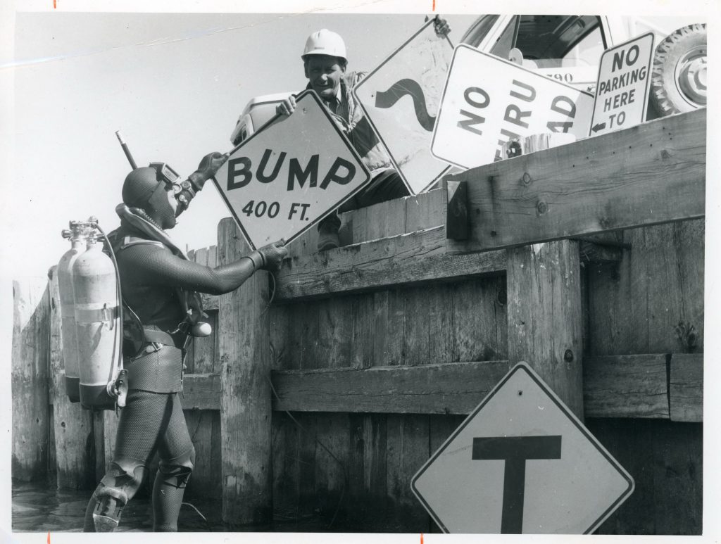 A scuba diver retrieves BC highways signage from Lake Okanagan during the 1960s.