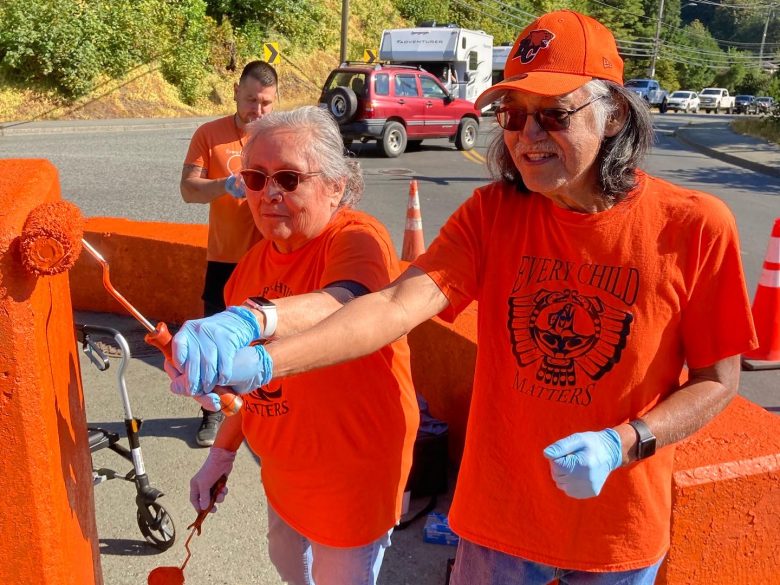 Two residential school survivors painting bridge orange