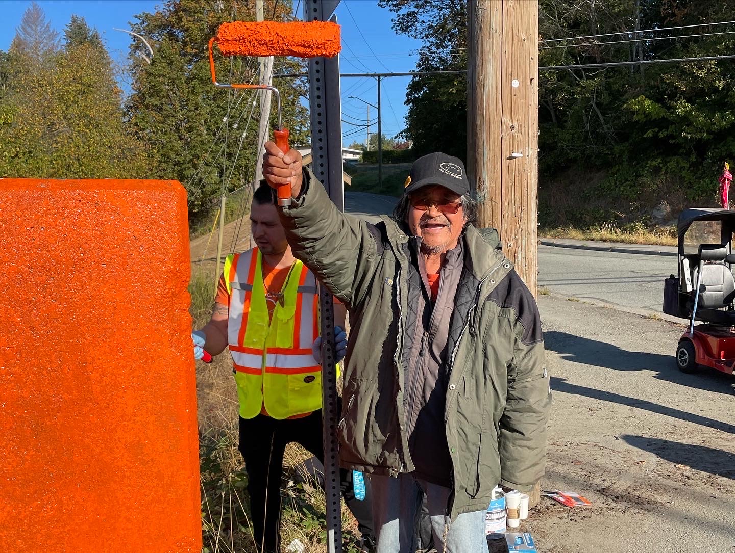 Residential school survivor Chuck August smiling while raising paint roller